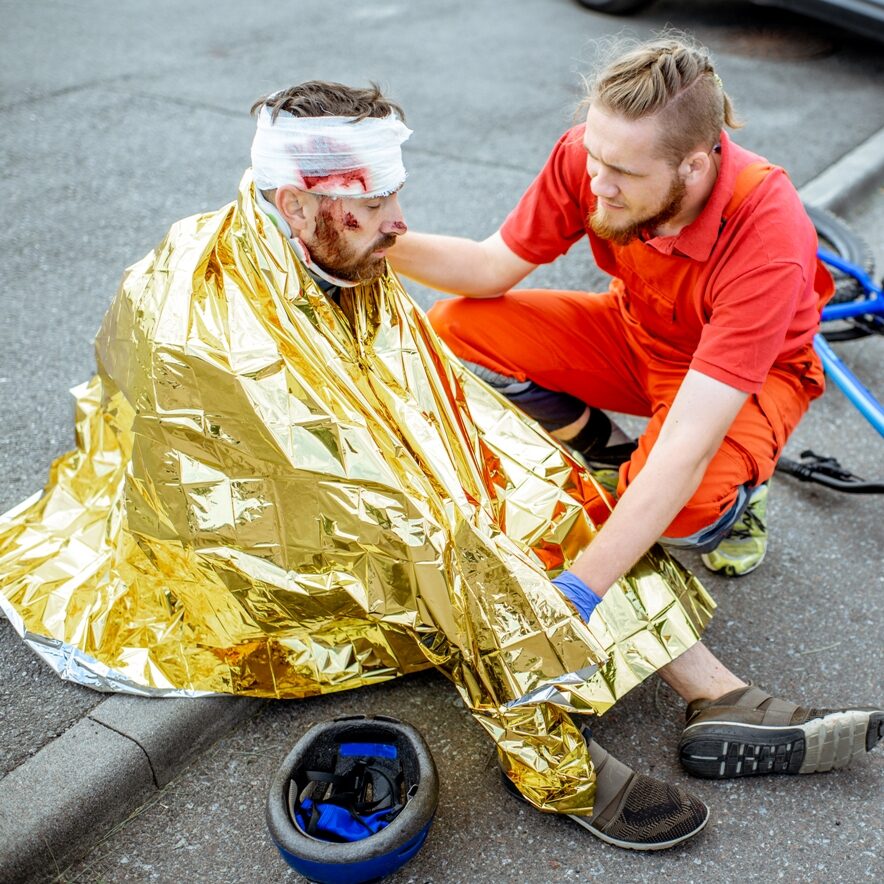 Ambluence worker covering injured man with thermal blanket, providing emergency care after the road accident